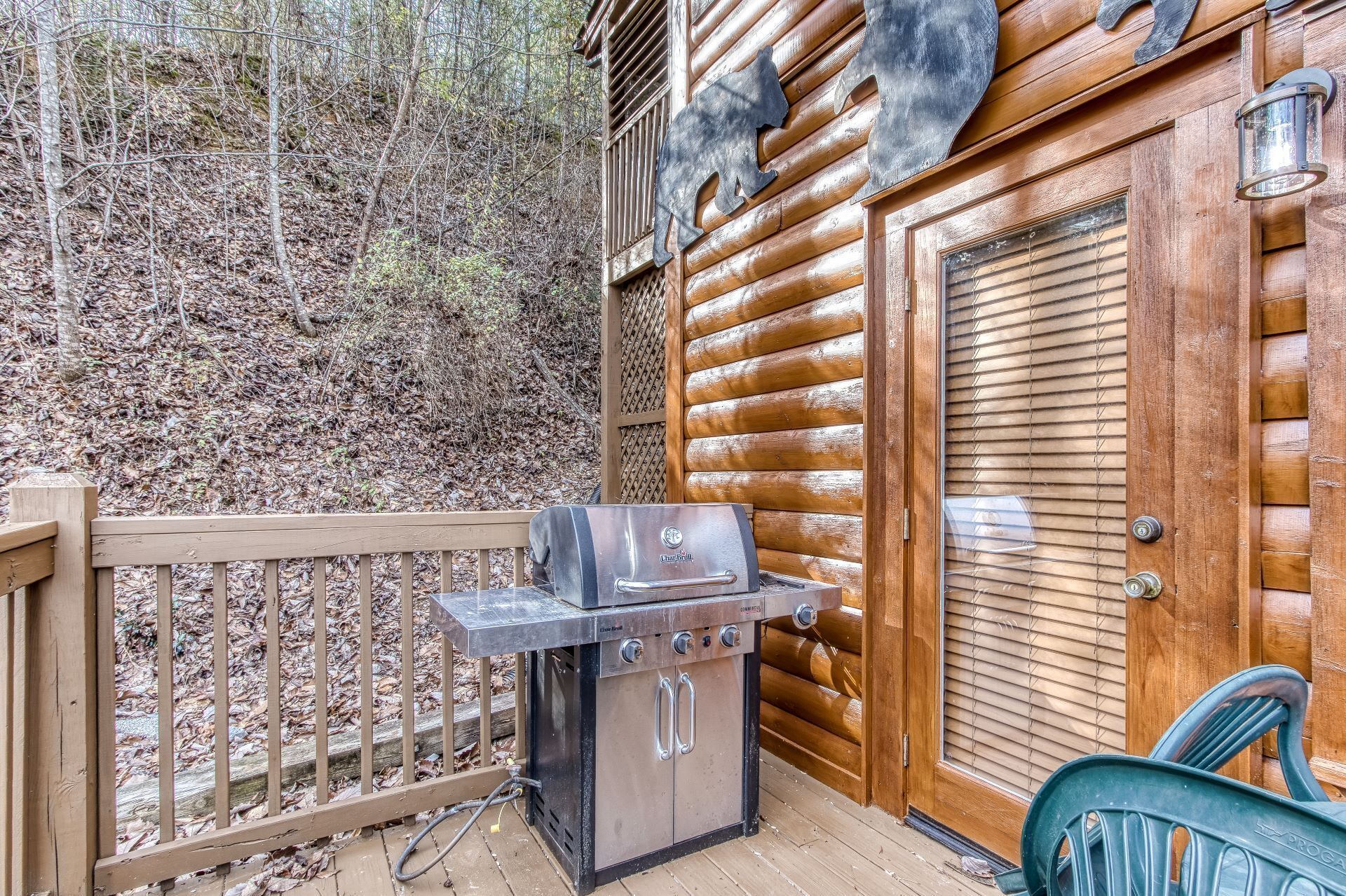 Una cabaña de madera con una parrilla afuera, una puerta con un recorte de oso y una terraza de madera.