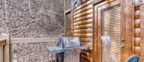 Una cabaña de madera con una parrilla afuera, una puerta con un recorte de oso y una terraza de madera.
