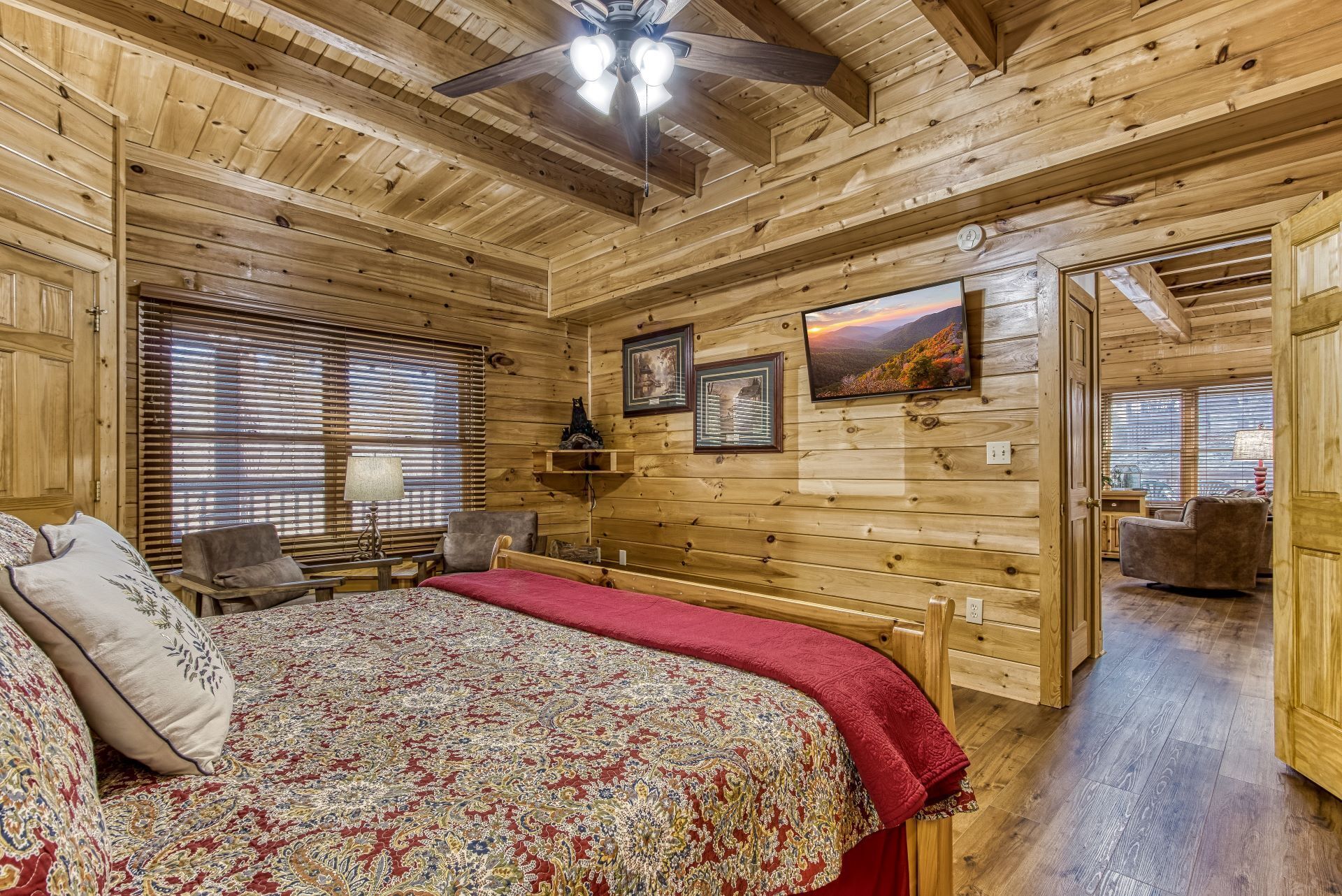 Un dormitorio de cabaña de madera con una cama, dos sillas, una mesa y un ventilador de techo.