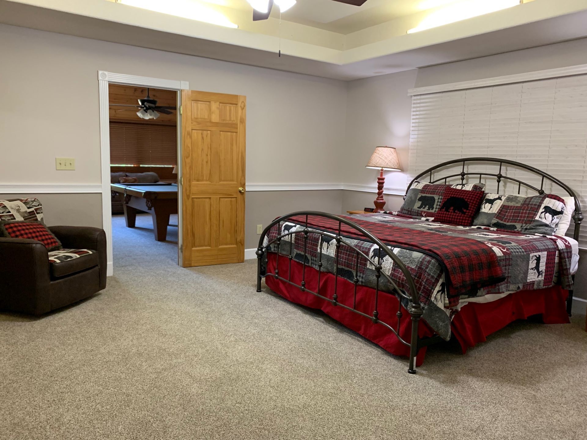 A bedroom with a bed, a chair, a desk, and a door leading to another room.