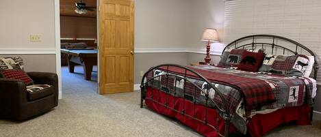 A bedroom with a bed, a chair, a desk, and a door leading to another room.