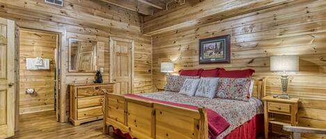 Ein Schlafzimmer einer Holzhütte mit einem Bett, Nachttischen, einer Kommode und einem Deckenventilator.