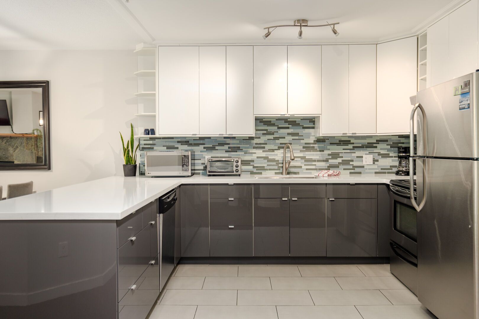 Eine moderne Küche mit weißen Schränken, einem Edelstahl-Kühlschrank, einer Mikrowelle, einem Toaster und einer gefliesten Spritzschutzwand.