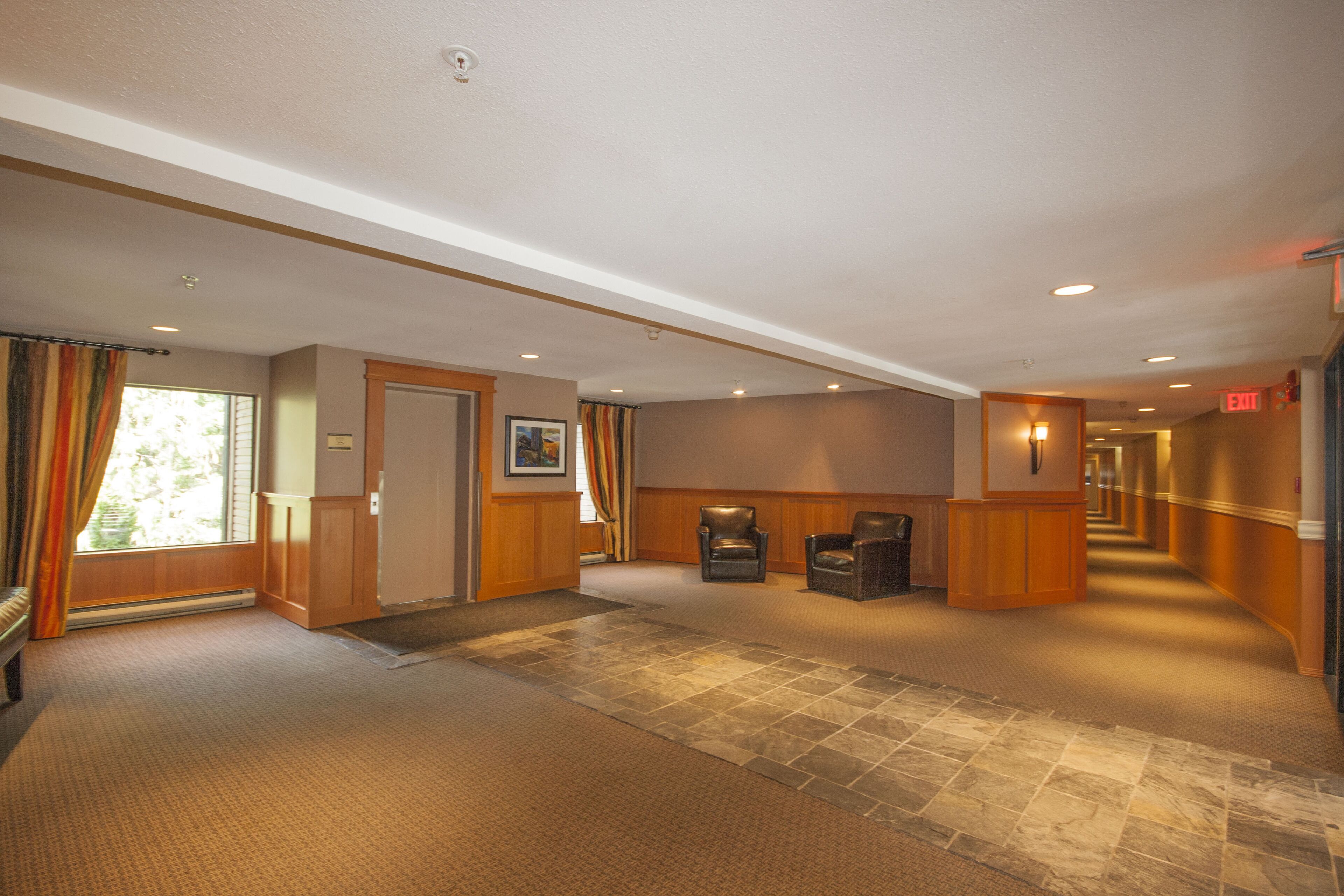 A hotel lobby with a carpeted floor, wooden paneling, a reception desk, and a door leading to a room.