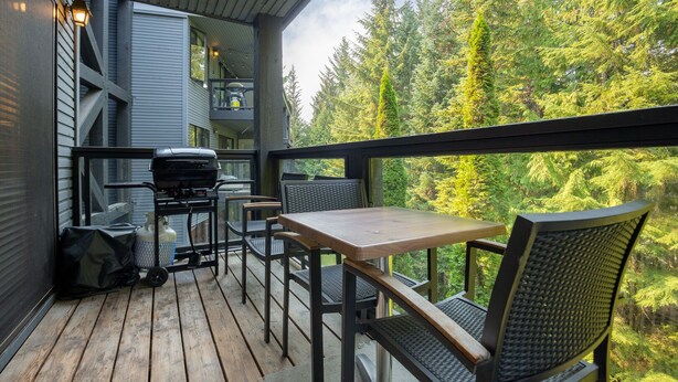An outdoor deck with a wooden table and chairs, a grill, and a view of a forest. - 2BR | Powderhorn | Near Blackcomb Ski Area | Double Sided Fireplace | Rooftop Hot Tub | Parking (Whistler)