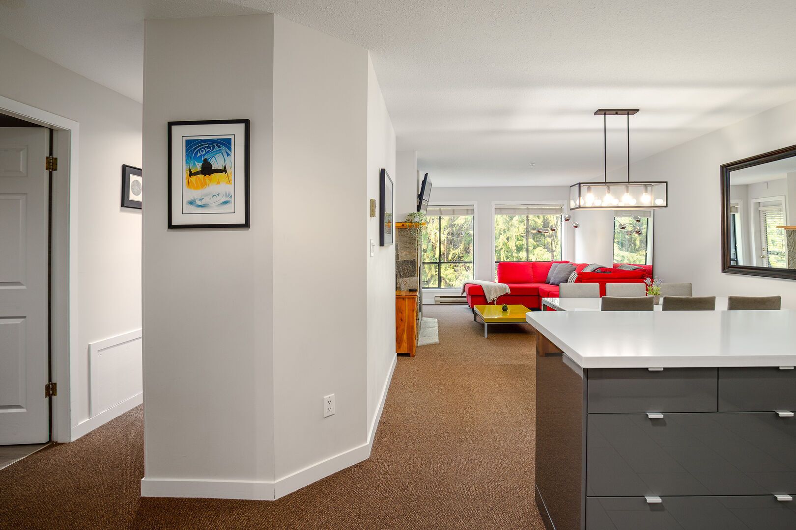 A modern living room with a red sofa, a dining area with a white table, and a kitchen with a large island.