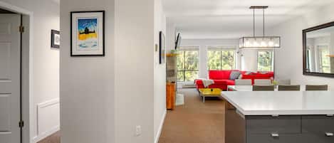 A modern living room with a red sofa, a dining area with a white table, and a kitchen with a large island.