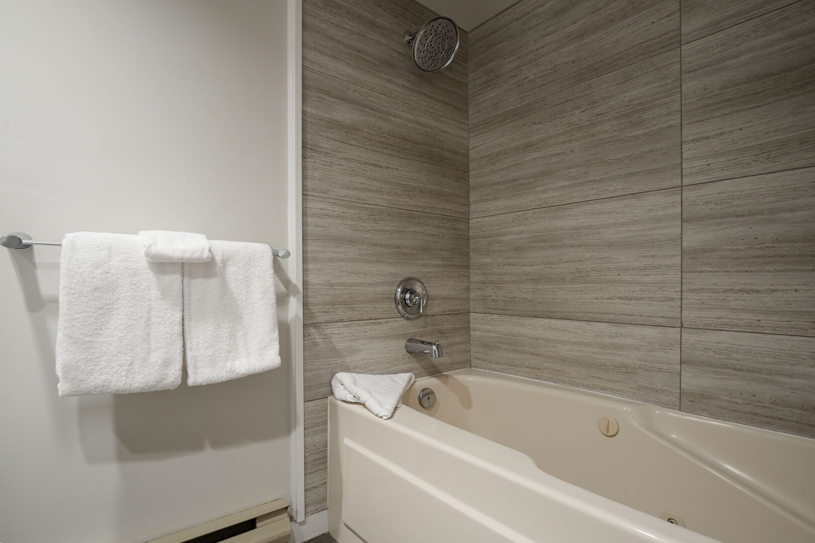 Un baño con bañera, cabezal de ducha y dos toallas colgadas en un perchero.