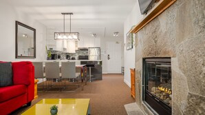 A modern living room with a red sofa, yellow coffee table, and a stone fireplace. - 2BR | Powderhorn | Near Blackcomb Ski Area | Double Sided Fireplace | Rooftop Hot Tub | Parking (Whistler)
