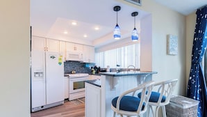 A modern kitchen with white cabinets, a built-in stove, and a bar area with two wicker chairs.