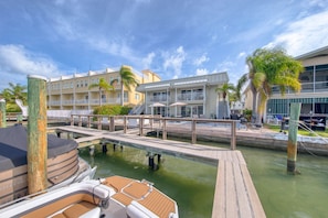 A marina with a dock, a boat, and a building with balconies and outdoor seating.