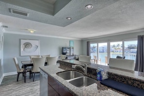 A modern kitchen with granite countertops, stainless steel sinks, and a dining area with chairs.