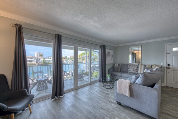 A spacious living area with a balcony, a grey sofa, a small table, and a chair.