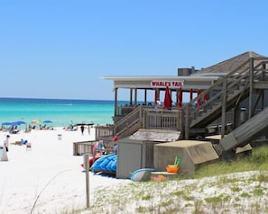 A beachside building with a sign reading "Whales Tail," featuring a wooden staircase and a covered seating area.