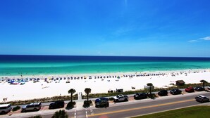 A beach with a road in the foreground, a clear blue sky, and the ocean in the background. - Majestic Sun 707A-1/1.5 bath condo with gulf views (Miramar Bch)