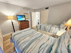 A bedroom with two beds, a dresser, a television, and a lamp. - Remodeled Beachside 4025 | Spacious Condo | Beachfront | Pool + Golf Cart Included (Miramar Beach)