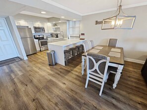 A modern kitchen with a central island, stainless steel appliances, and a dining area with a chandelier. - JAN/ FEB now open!!  Beachside 4025 | Spacious Condo | Beachfront | Pool + Golf Cart Included (Miramar Beach)