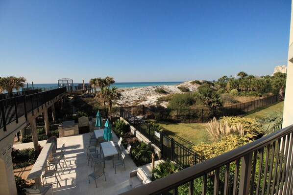 A balcony with a view of a beach, outdoor seating, and a grill area.
