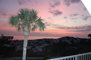 Eine Palme vor einem Sonnenuntergang, mit Strand und einer Holzkonstruktion im Hintergrund.