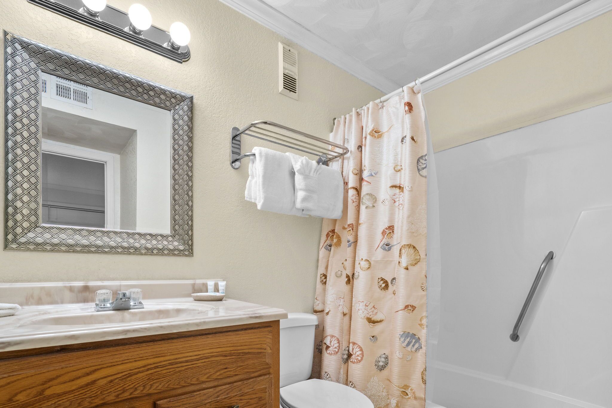 A bathroom with a vanity, mirror, towel rack, shower curtain, and a handrail.