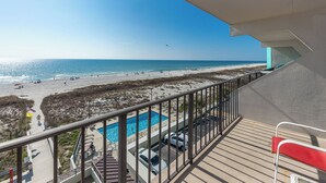 Ein Balkon mit Pool, Blick auf den Strand und einem eingezäunten Bereich mit Liegestühlen.