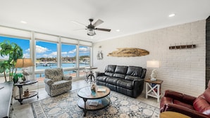 A spacious living room with a large window, a ceiling fan, a leather sofa, a patterned rug, and a view of a pool. - Beautiful condo located on the ship channel and in the heart of Port Aransas! Th (Port Aransas)