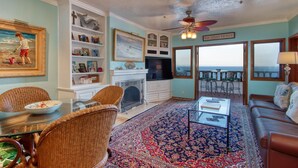 A living room with a fireplace, a dining table with chairs, a sofa, and a large window with a view. - H249: Gorgeous Villa,NO STEPS,Panoramic Ocean Views,Private Balcony, 6-Seat Cart (Avalon)
