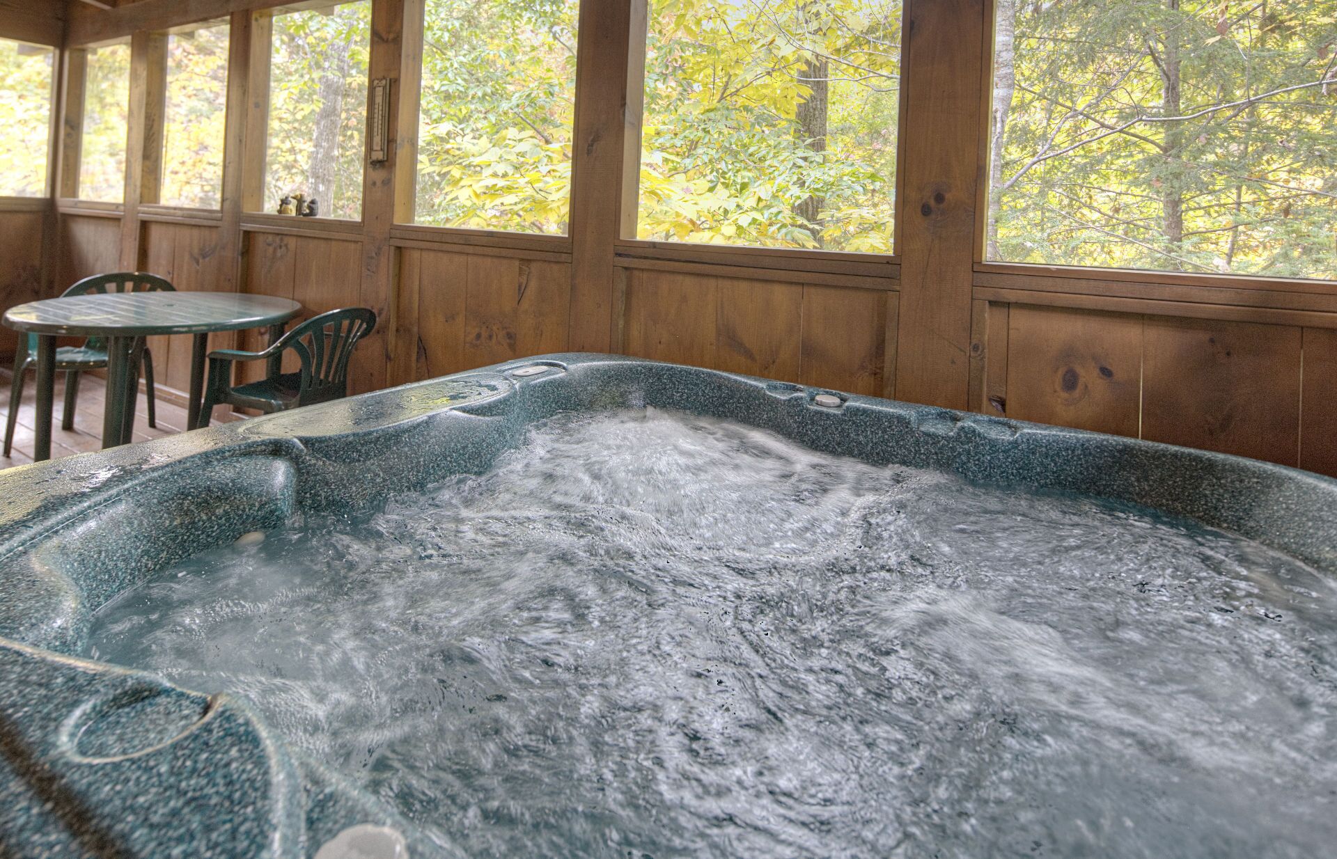 A hot tub in a wooden cabin with a view of autumn trees.