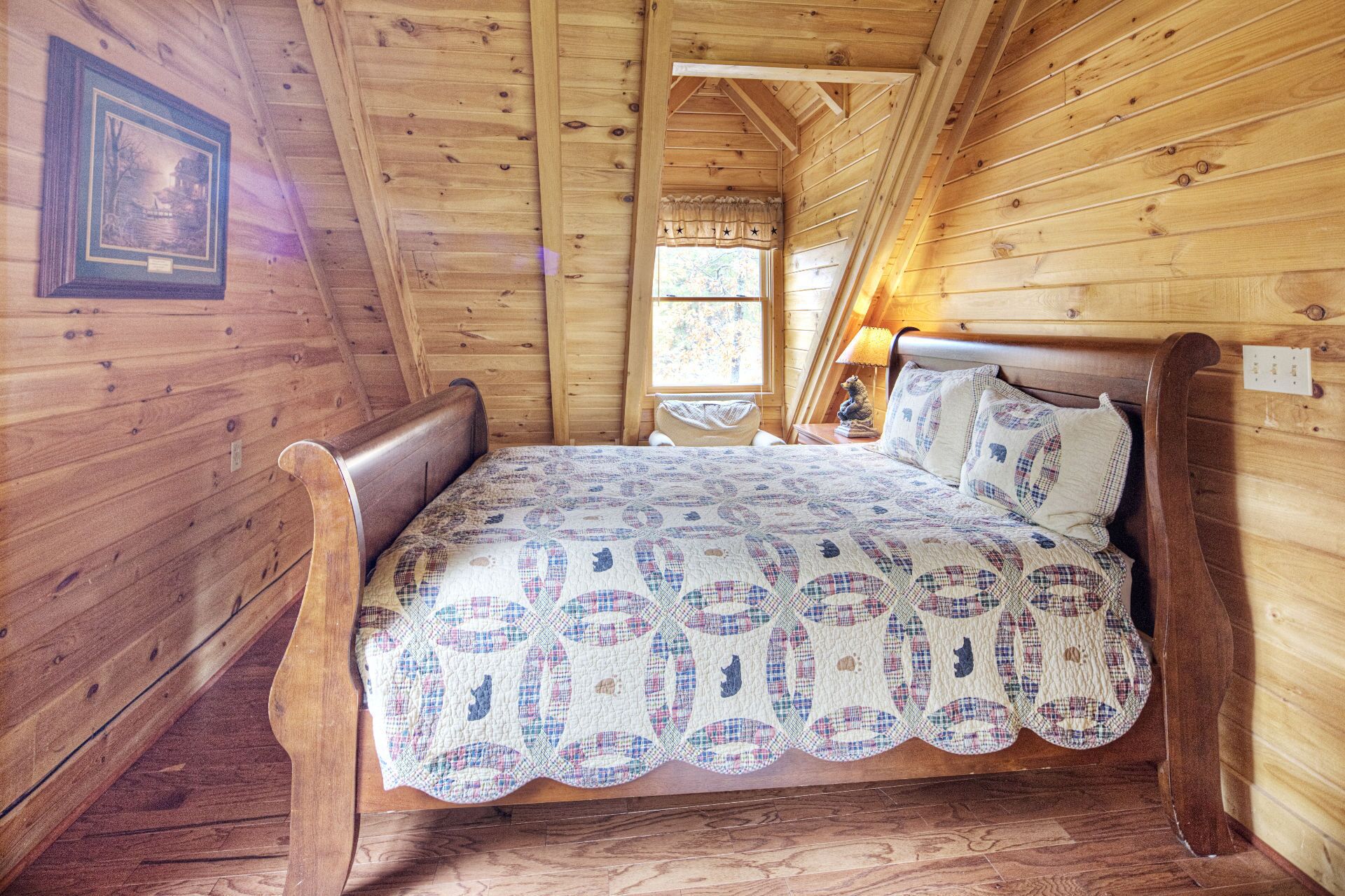 A wooden cabin bedroom with a bed, a window, and a picture on the wall.