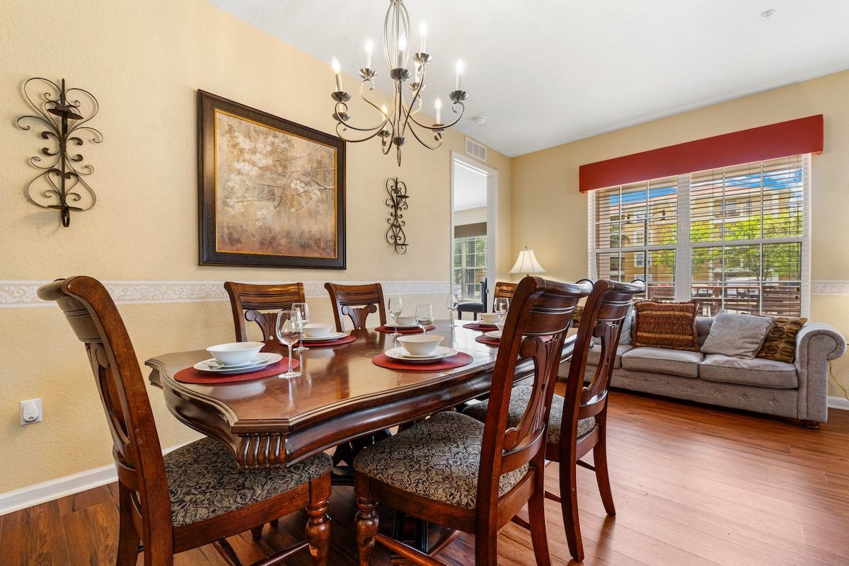 A dining area with a wooden table set for six, surrounded by upholstered chairs with patterned cushions.