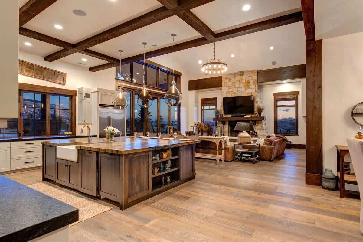 A spacious kitchen with a large island, wooden beams, and a stone fireplace.