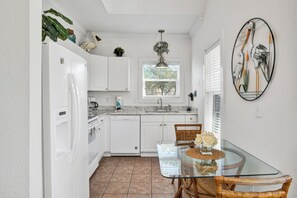 A modern kitchen with white cabinets, a glass dining table, and a window with blinds.