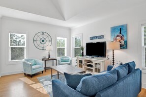A living room with a television, two armchairs, a coffee table, and a painting of a boat.