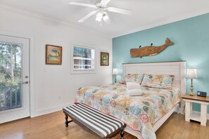 A bedroom with a bed, a bench, a ceiling fan, and a wall-mounted fish decoration. - Purple Parrot 2nd Floor Condo w Loft (Pensacola)