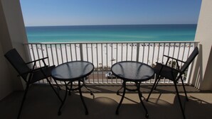 A balcony with two tables and chairs, overlooking a beach with umbrellas and people.