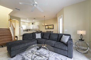 A modern living room with a sectional sofa, a glass coffee table, a chandelier, and a dining area in the background. - Pool Home with Spa & Games Room in Gated Community Near WDW (Davenport)