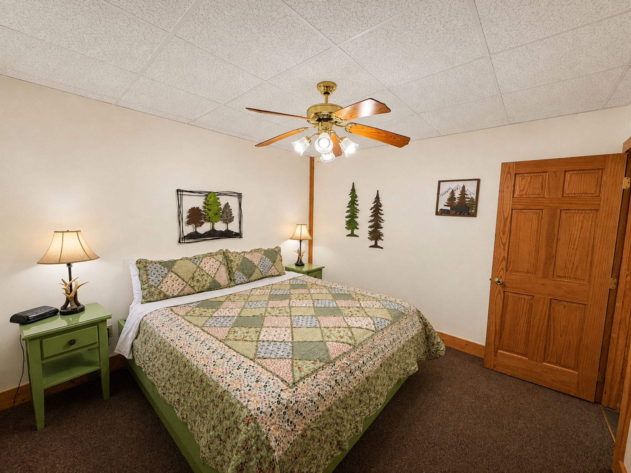 A bedroom with a bed, two nightstands, a ceiling fan, and a wooden door.