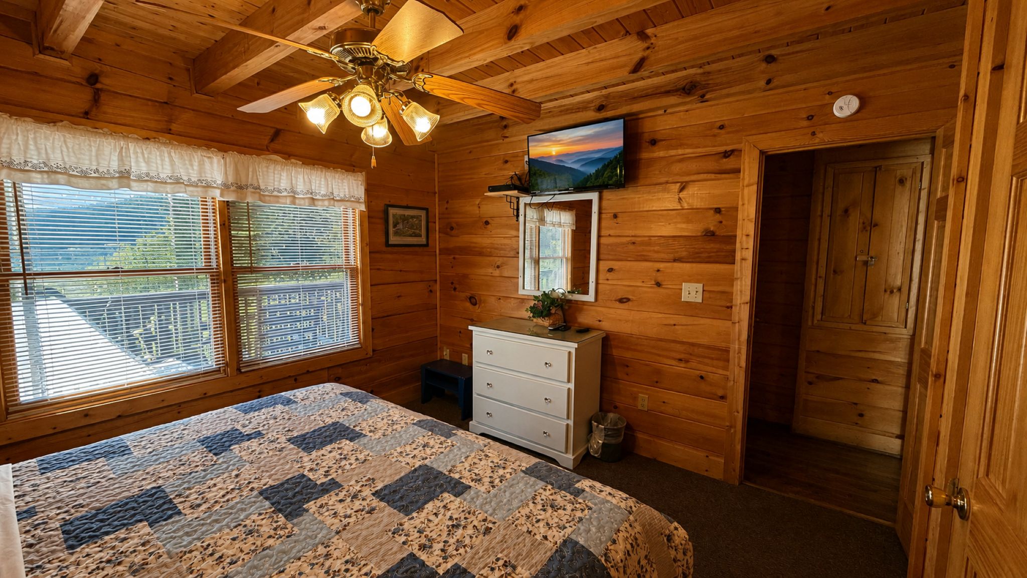 Une chambre dans une cabane en bois, avec un lit, une commode et un ventilateur de plafond.