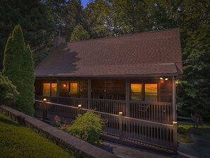 Une cabane dotée d’une véranda, d’une cheminée et offrant une vue sur la forêt environnante.