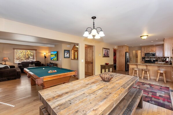 A spacious living room with a pool table, a wooden coffee table, and a bar area with stools.