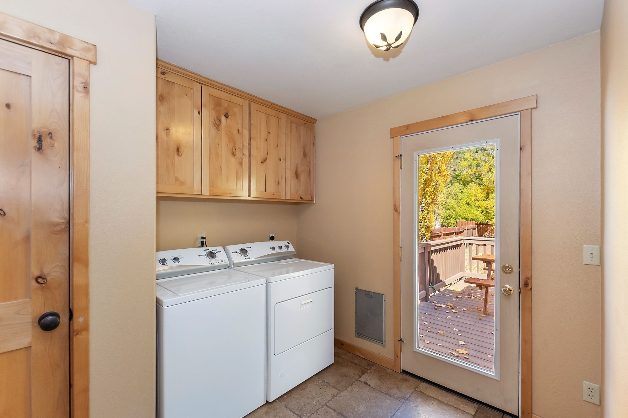 A laundry room with wooden cabinets, a washer and dryer, and a door leading to an outdoor deck.