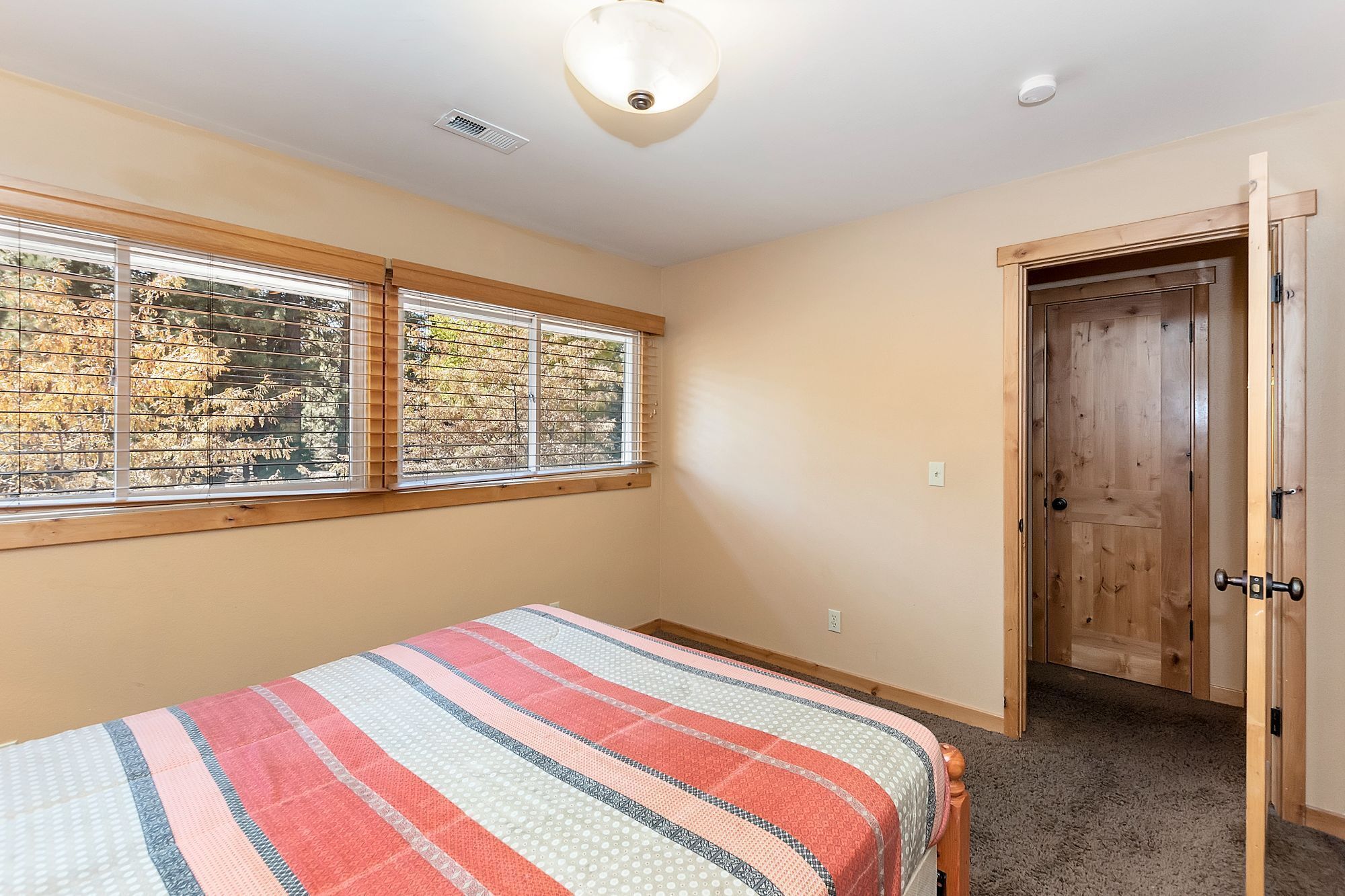 A bedroom with a bed, a window with blinds, a door, and a ceiling light.