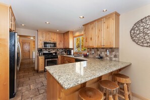 A kitchen with wooden cabinets, granite countertops, a built-in microwave, and a large island with stools.