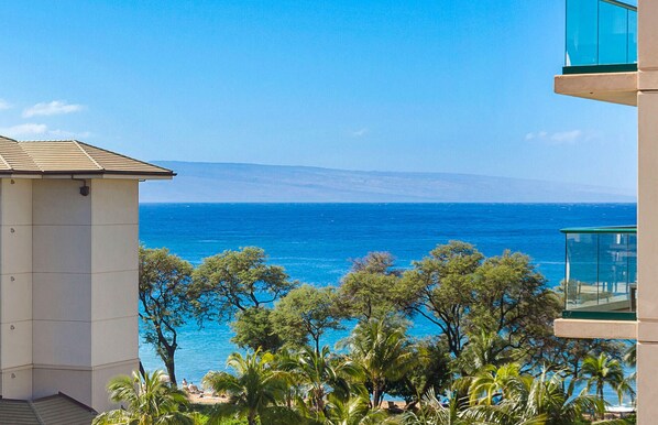 Vista sulla costa da un balcone con vista sul mare, con un edificio e alberi sullo sfondo.