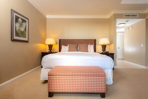 A hotel room with a large bed, two bedside tables with lamps, a framed picture on the wall, and a carpeted floor.