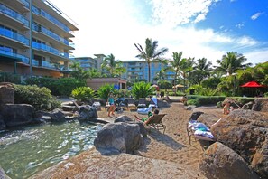 A resort pool area with lounge chairs, a water feature, and palm trees. - Honua Kai | Ocean View Studio | Car Incl. w/ 6+ Nights | HKH-423 by KBM (Lahaina)