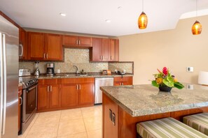 A modern kitchen with wooden cabinets, a granite countertop, and a built-in dishwasher. - Honua Kai | Ocean View Studio | Car Incl. w/ 6+ Nights | HKH-423 by KBM (Lahaina)