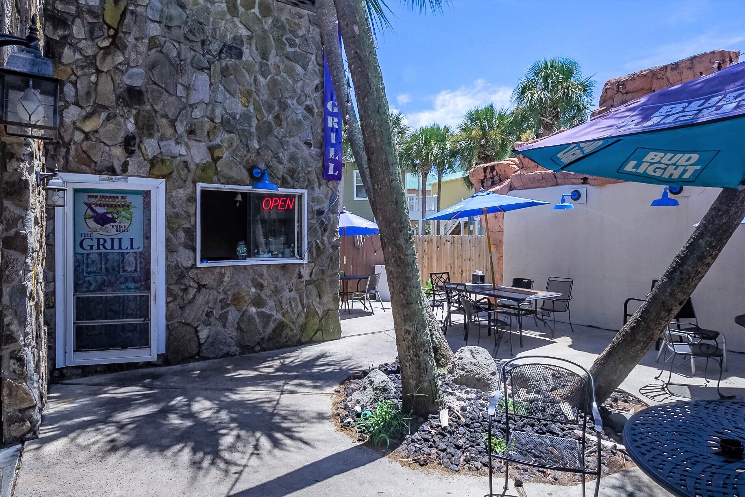 A stone building with a sign for 'The Grill' and outdoor seating with Bud Light umbrellas.