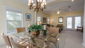 A spacious dining area with a glass table surrounded by wicker chairs, a chandelier, and a ceiling fan. - Oceanfront Opulence: Vacation Home with Amazing Pool, Beach Just Moments Away (Pensacola)