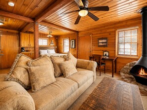 Interior acogedor de una cabaña con techo de madera, un sofá con cojines estampados, una chimenea y un comedor.